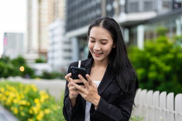 Fototapeta premium Asian young businesswoman chatting on smartphone while standing in city.