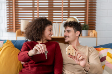 Fototapeta premium Hispanic Latina young couple holding a key and small wooden house model. 