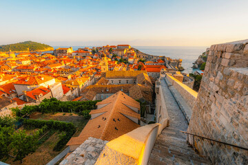 Obraz premium Golden hour panorama of Dubrovnik's historic fortifications and old port at dusk, sunlight on ancient stone walls and Mediterranean architecture in Croatia
