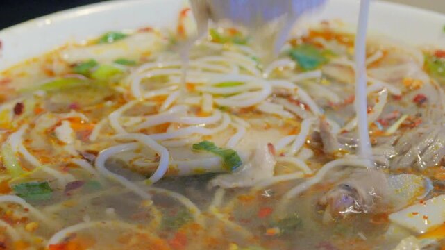 Close up action shot of wooden chopsticks picking up ingredients from a hot bowl of traditional B&uacute;n b&ograve; Huế soup