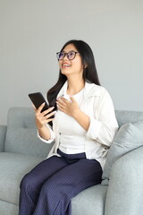 Obraz premium A happy young woman, feeling relieved or fortunate, holds her chest and looks up, celebrating a victory or receiving a message containing good news.