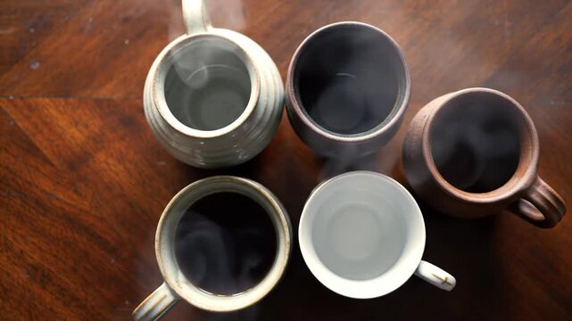Five steaming mugs of coffee and tea on a wooden table, top view