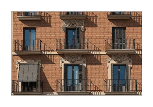Detailed red brick apartment building facade with ornate stone architectural carvings above windows, black metal balcony railings, window shutters, and sharp shadows from sunlight.
