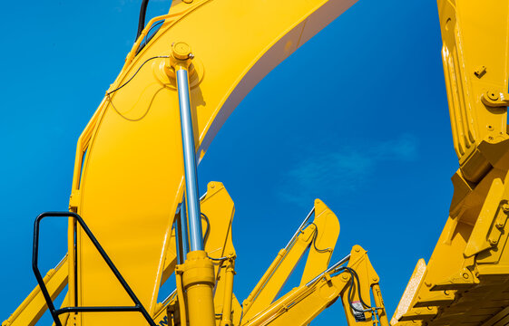 Yellow backhoe with hydraulic piston arm against clear blue sky. Heavy machine for excavation in construction site. Hydraulic machinery. Huge bulldozer. Heavy industry