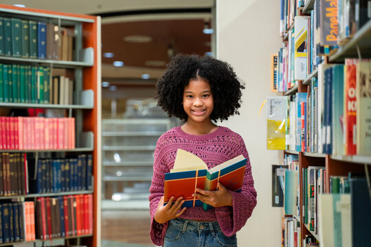 Portrait of African American young girl holding a book in quiet library. 