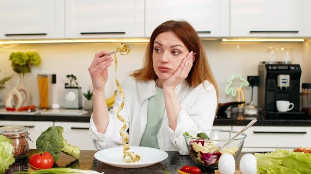 Middle-aged woman feels sad holding measuring tape in home kitchen during weight loss diet plan. Young adult girl fights cravings builds willpower for healthy eating nutrition meal planning goals fit.
