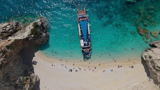 Drone footage ascending above a cruise ship anchored at a secluded beach on Ithaca Island, Greece. Crystal-clear turquoise waters, white cliffs and a remote Mediterranean shoreline create