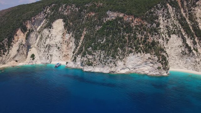 Drone aerial view of a secluded beach cove on Ithaca Island, Greece. Crystal-clear turquoise waters meet dramatic white limestone cliffs along the Ionian coastline