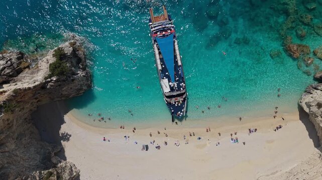 Top-down drone view of a tourist excursion ship anchored at a secluded beach on Ithaca Island, Greece. Crystal-clear turquoise water