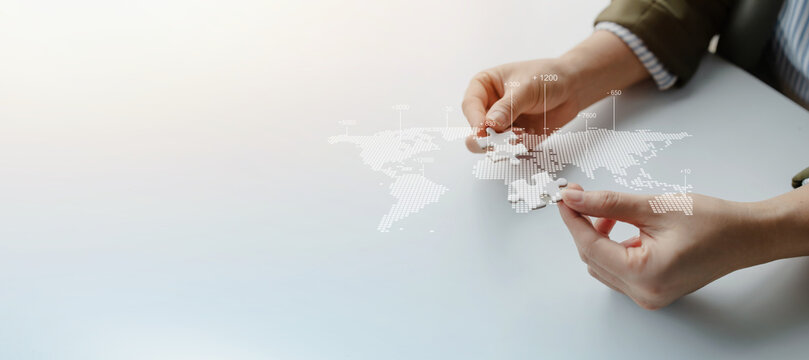 Hands assembling puzzle pieces over a digital world map, symbolizing global business expansion, international collaboration, worldwide connectivity, market integration, and strategic partnerships.