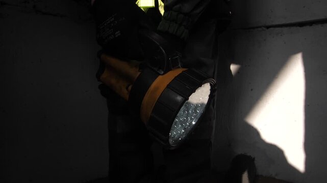 Man worker in uniform shining lit flashlight on construction site at work.