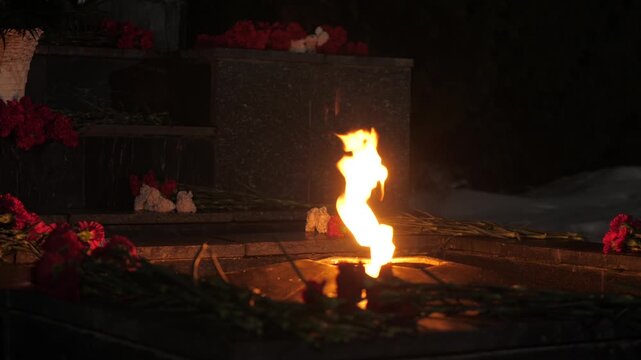 Flowers at eternal flame near war heroes monument in winter evening in city.