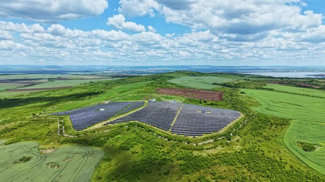 Aerial view curved solar panel array showing spiral rows of reflective modules across rolling hills, sunlight glinting on modules, utility scale clean energy