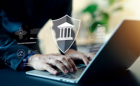 Businessman using laptop with digital shield icon protecting bank symbol. Concept of banking security, financial technology, online data protection, cyber security, and safe digital transaction.