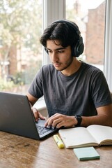 Fototapeta premium Teenage boy with headphones focusing on his laptop in a home study setup for online education, student lifestyle and remote learning campaigns with copy space