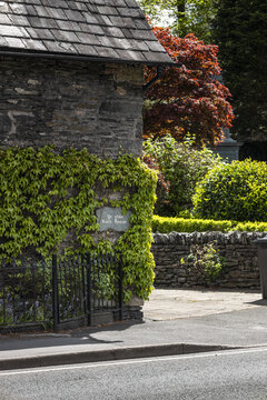 View of the historic Ye Olde Bath House stone building covered in lush green ivy with a slate roof and stone wall in Windermere, England, United Kingdom.