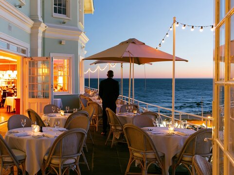 Luxury coastal restaurant terrace at sunset with a person looking at the sea for travel promotion, fine dining advertising and vacation hospitality background