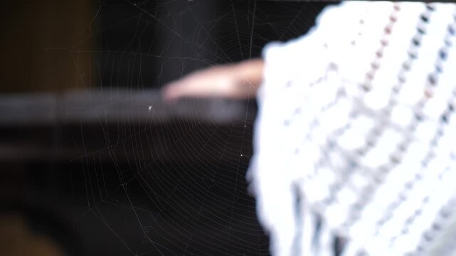 View through spider web to woman on balcony covered white knitted blanket.