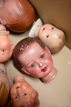Collection of vintage doll heads scattered in a cardboard box, some with chipped paint