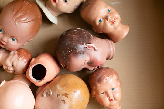 Collection of vintage doll heads scattered in a cardboard box, some with chipped paint