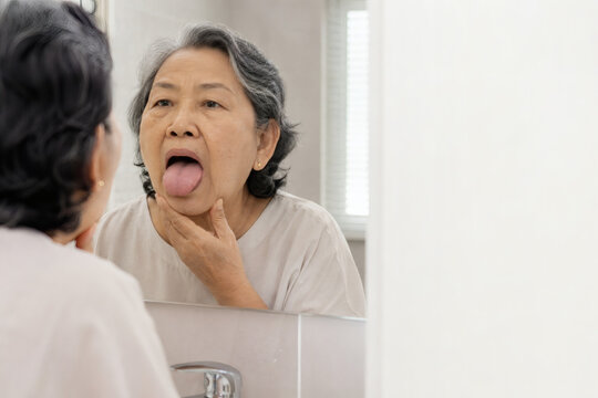 Senior Woman Inspecting Tongue for Dry Mouth Symptoms in Mirror
