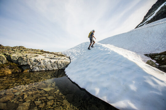 Hiker ascends a snowy slope in summer mountains