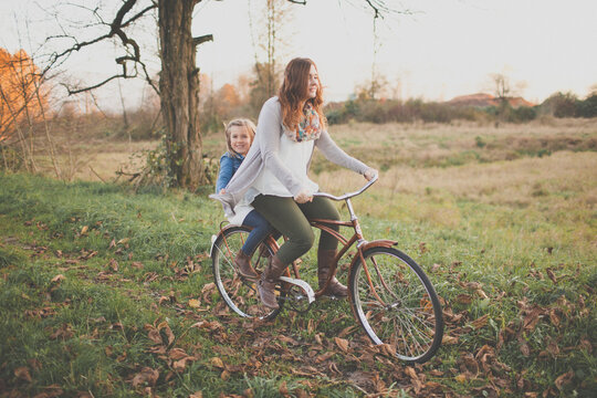 Happy mother and daughter riding bicycle in autumn field