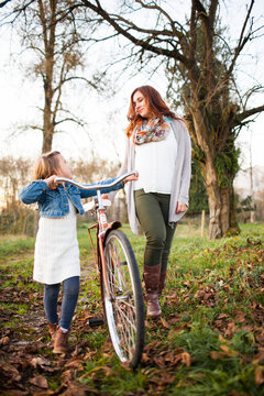 Mother and daughter walking with a bicycle outdoors