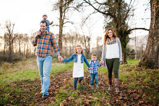 Young family holds hands walking through woods