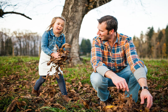 Young girl playfully gathers autumn leaves with her dad