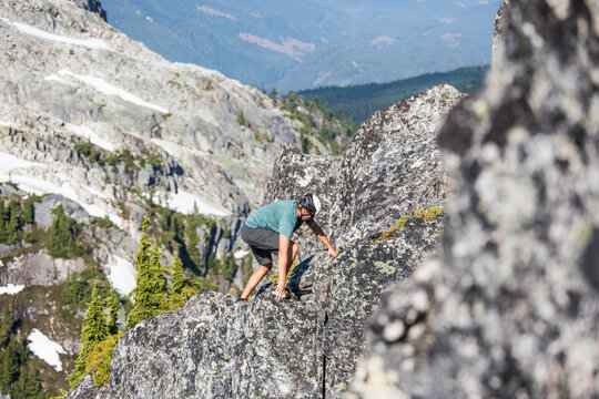 Man in helmet scrambles up a rocky mountain ridge