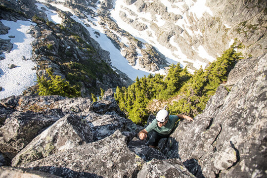 Man in helmet rock climbing up a mountain face