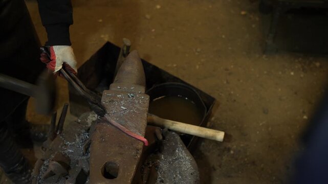 Two men blacksmiths working in blacksmith shop on forming metal with hammers.