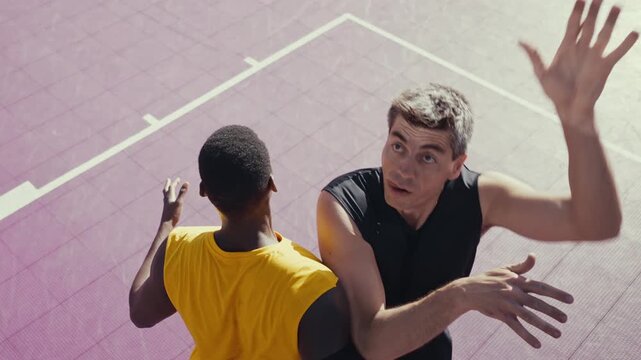 Two diverse men are intensely playing basketball on a vibrant purple outdoor court, with one player dunking the ball into the hoop while the other defends