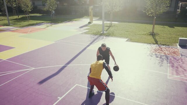Two diverse men are intensely playing basketball on a vibrant purple outdoor court, with one player dunking the ball into the hoop while the other defends