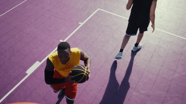 Two diverse men are intensely playing basketball on a vibrant purple outdoor court, with one player dunking the ball into the hoop while the other defends
