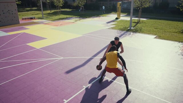 Two diverse men are intensely playing basketball on a vibrant purple outdoor court, with one player dunking the ball into the hoop while the other defends