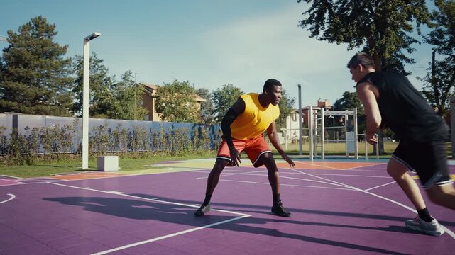 Two young male athletes are actively competing during a streetball game, dribbling the ball and playing defense on a vibrant outdoor basketball court, showcasing sport, fitness, and teamwork