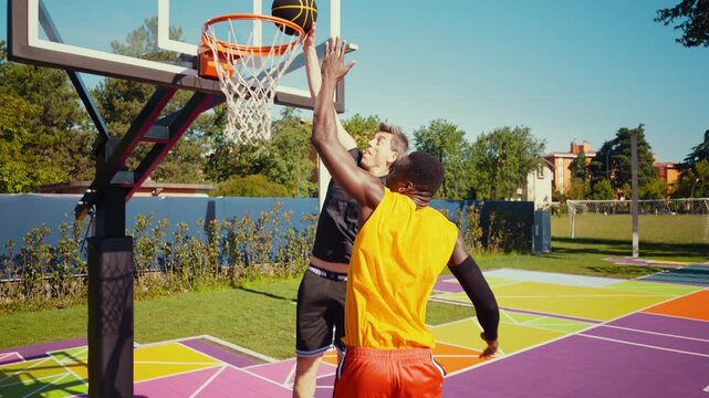Two diverse basketball players compete on a vibrant purple outdoor court, one soaring for a dunk from above, capturing athletic training, energy, and dynamic urban streetball action