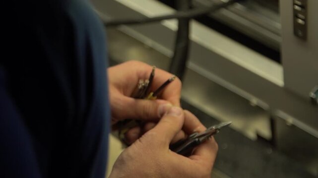 Man worker electrician cleans ends of wires with pliers for connection.