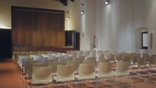 Softly defocused meeting room with rows of chairs and a wooden stage, interior; background backdrop copyspace calm.