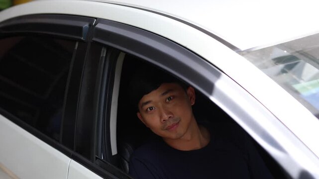 Asian man in his car slide car mirror and look at camera with happy smile
