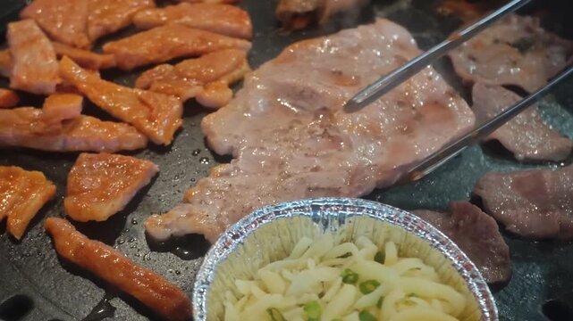 Close up of Korean barbecue tabletop grill with marinated pork beef slices traditional rolled egg gyeran mari and melted cheese cup sizzling