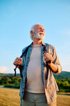 Happy senior man smiling while holding backpack straps, enjoying outdoor adventure, health, and freedom in retirement