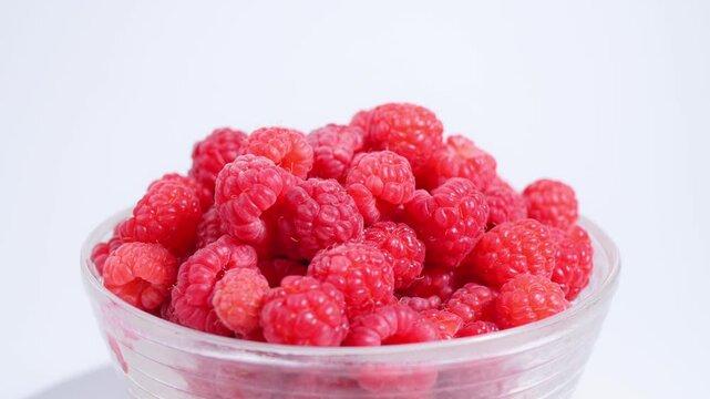Ripe raspberries in white glass bowl rotate against white background with space for text. Organic healthy food concept, healthy summer raspberries. 