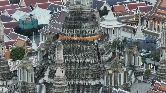 Wat Arun in Bangkok, Thailand. The iconic spire is partially covered by scaffolding and green netting, indicating ongoing preservation efforts.