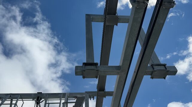 Industrial metal framework features overhead cables and pulleys against a clear blue sky, highlighting mechanical components in continuous motion