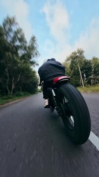 Rear low angle tracking shot of a custom cafe racer motorcycle cruising on a scenic winding road through the countryside.