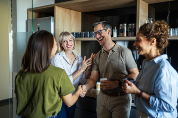 Naklejka premium Diverse colleagues shaking hands and laughing in office kitchen