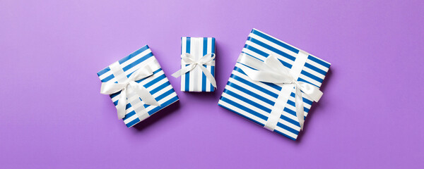 Fototapeta premium wrapped Christmas or other holiday handmade present in paper with White ribbon on purple background. Present box, decoration of gift on colored table, top view